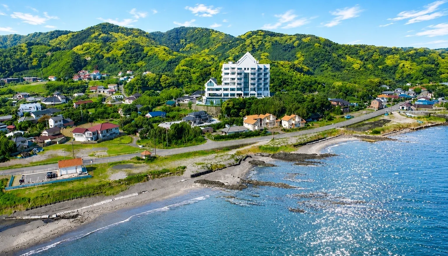 The exterior of New WestPeninsula Hotel on a green hilltop, with a view of Tateyama Bay